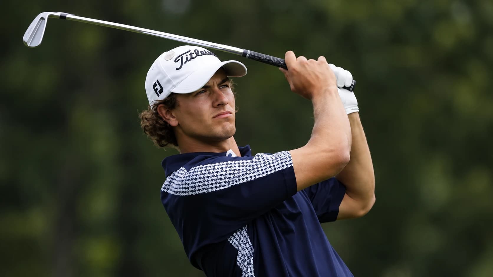 Een golfer met witte pet kijkt zijn ijzerslag na