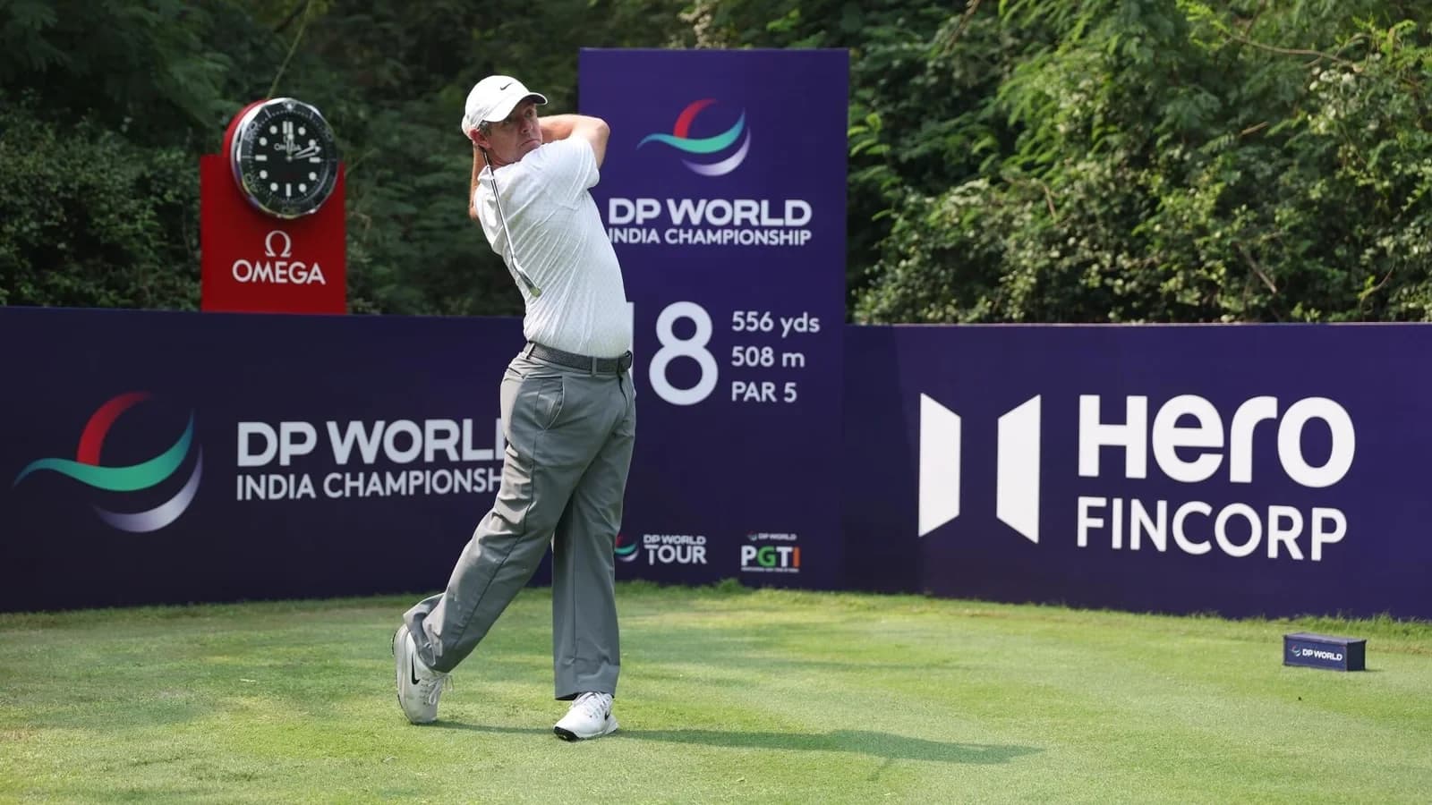 Rory McIlroy hits a tee shot in wide grey trousers at the 2026 DP World India Championship