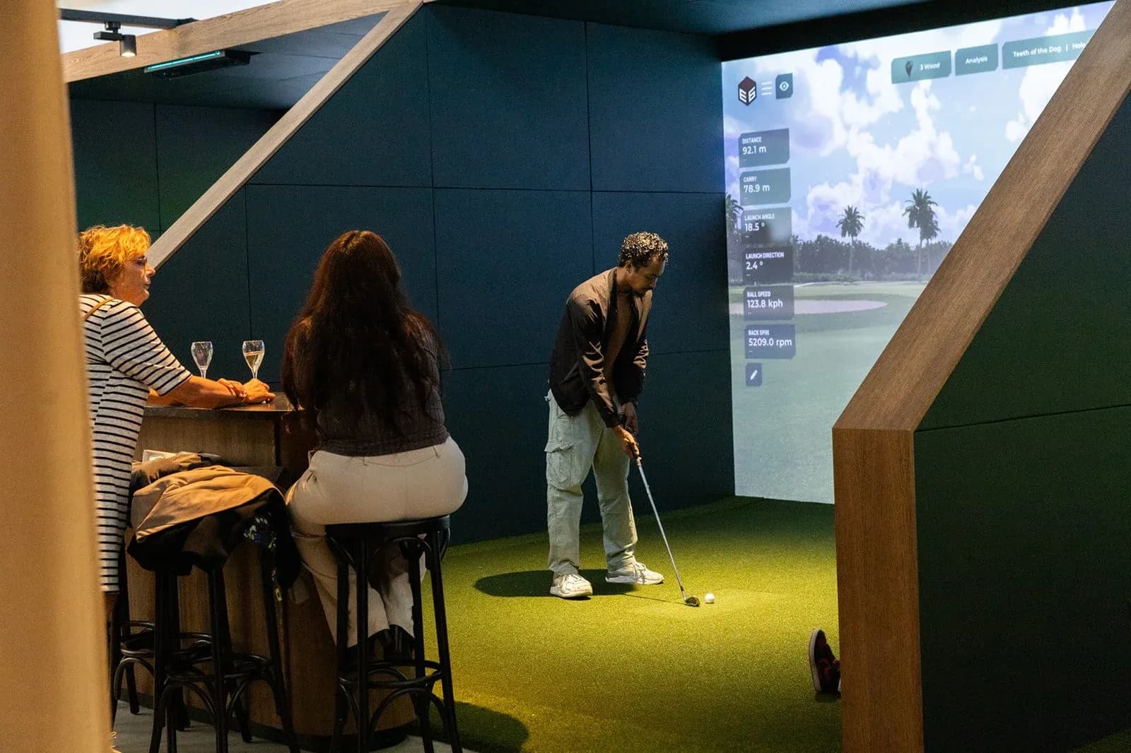 A golfer in one of the simulator bays at Club Birdies, with friends at the bar beside it