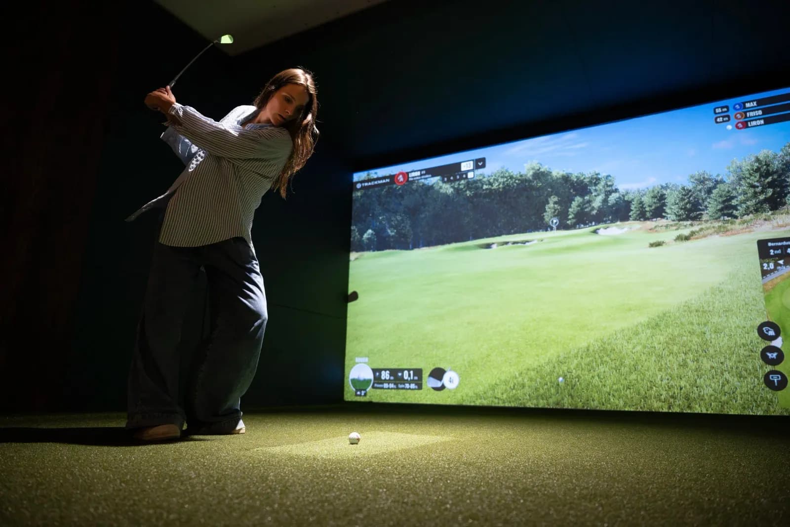 Een golfer midden in de swing in een bay van NEXT Golf