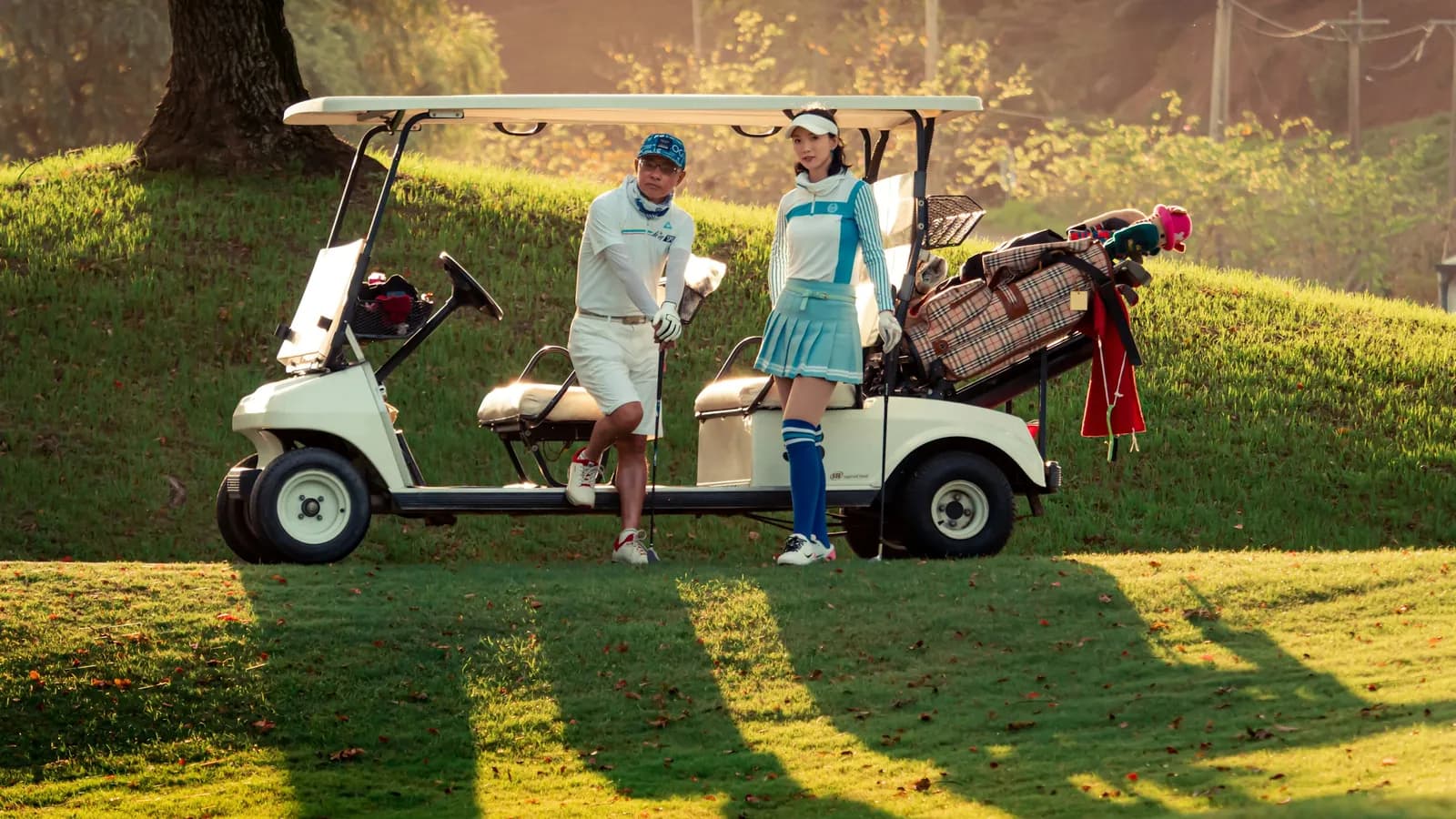 A man and a woman standing next to a golf cart in warm evening light