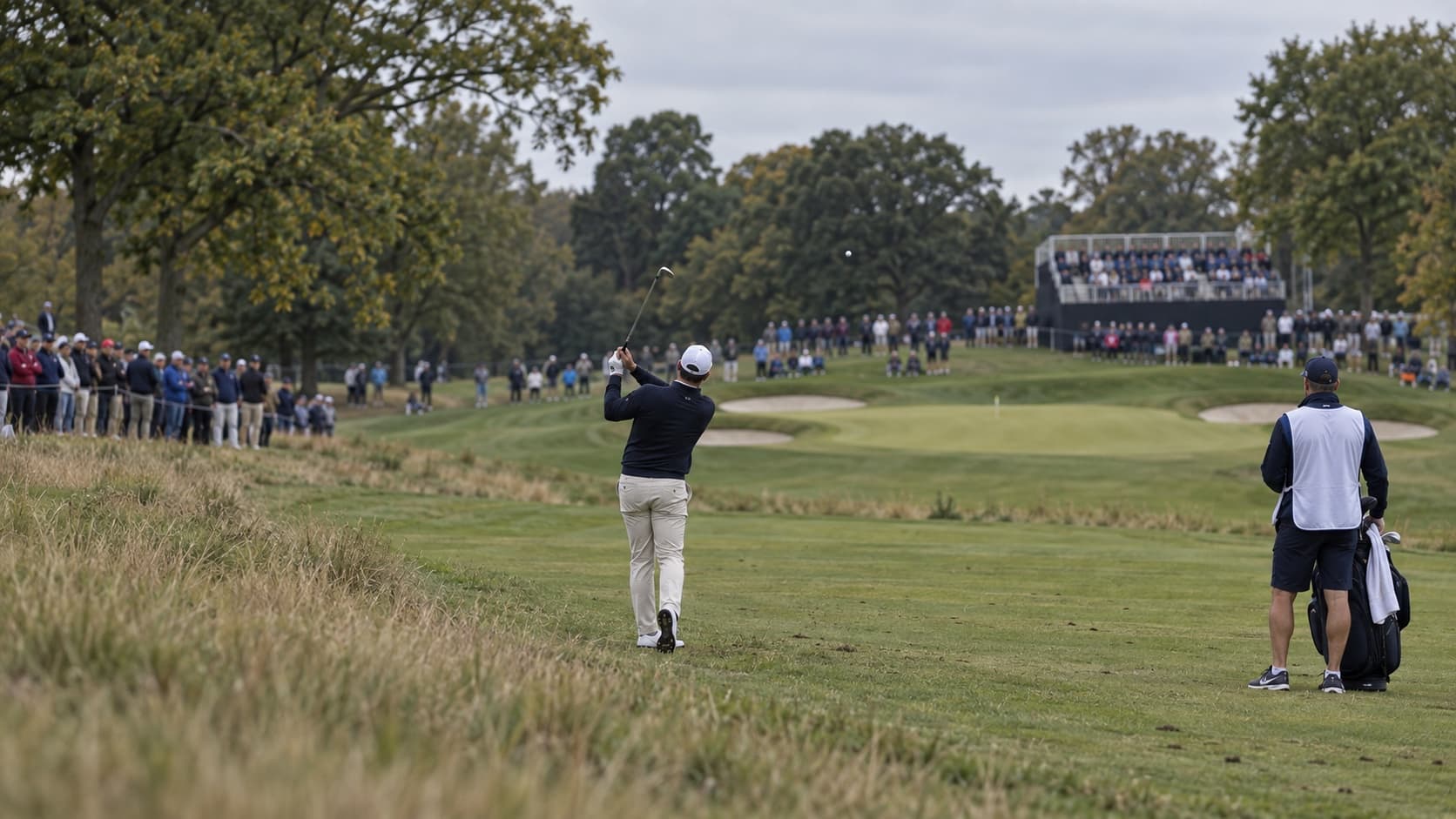 A golfer watches his iron shot as spectators line the fairway